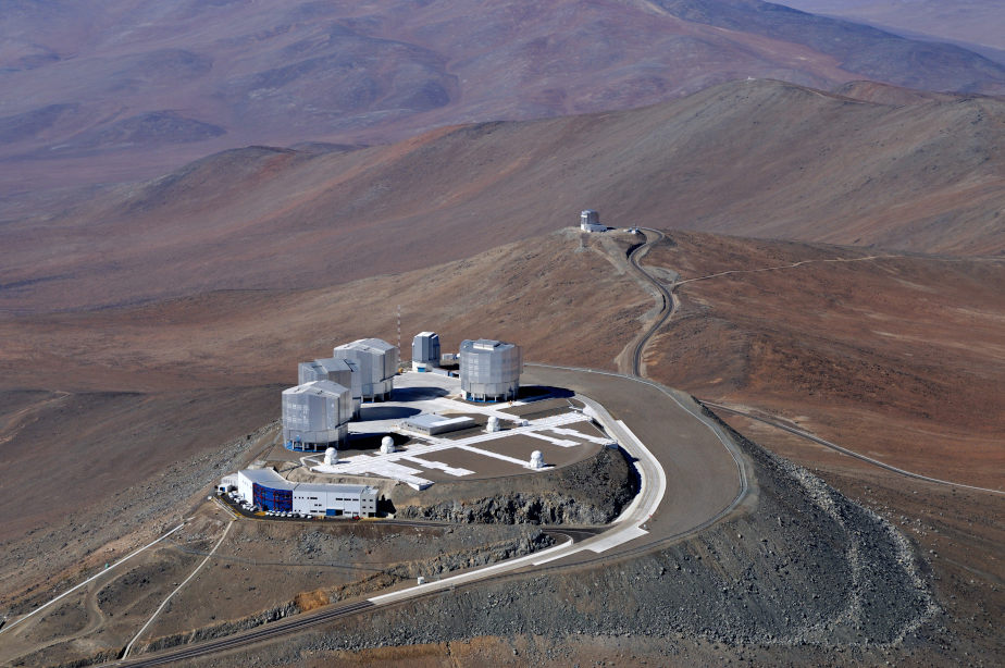 Die farbige Abbildung zeigt eine astronomische Forschungsstation auf einem Berg, welcher von einer Wüstenlandschaft umgeben ist.