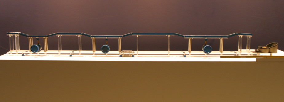 The photo shows a kind of marble run, which is placed on a beige base against a brown background. At three places along the linear tracks are handles that can be turned.