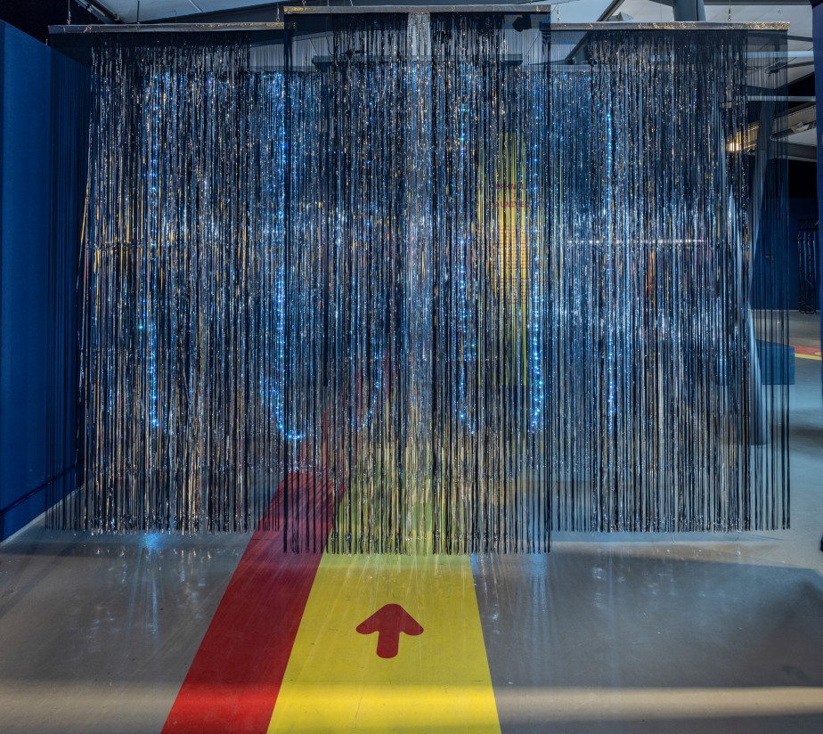 You can see a curtain made of silver tinsel. There is a red and a yellow stripe stuck to the floor and a red arrow pointing towards the curtain.