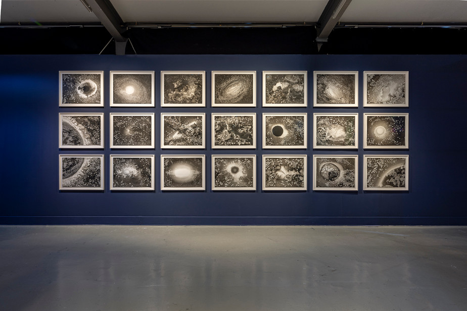 In front of a dark blue wall we see three by seven picture frames. The pictures themselves are black and white, depicting shapes and structures reminiscent of images from the cosmos with stars and galaxies.