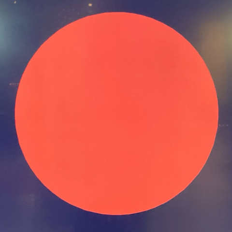 Das quadratische Bild zeigt einen großen roten Kreis vor dunklem Hintergrund.